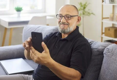 Smiling senior man using smartphone on sofa at home during video call session Stock Photos
