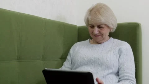 Smiling senior woman using tablet on sofa, digital lifestyle Stock Footage 328533134