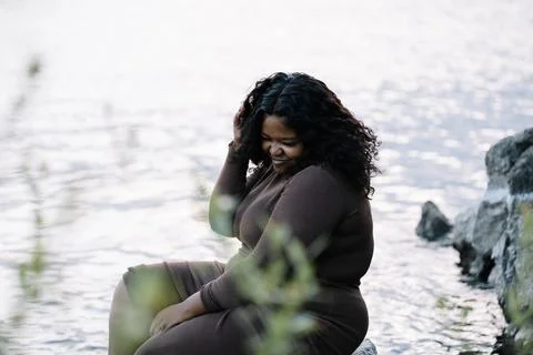 Smiling shy curly plump interracial African American dark skin woman sitting by Stock Photos