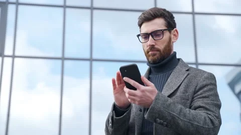 Smiling smart businessman typing message using phone standing on urban street Stock Footage 163300410