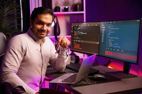 Smiling smart IT developer looking at camera while working on laptop. Surmise. Foto stock