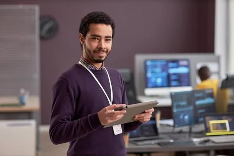Smiling software engineer holding digital tablet while standing in tech office Stock Photos
