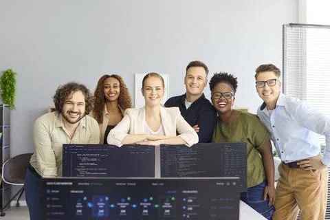 Smiling software team portrait behind monitors in contemporary startup office Stock Photos