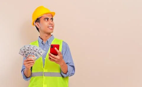 Smiling Southeast Asian construction worker in hard hat and safety vest hol.. Stock Photos
