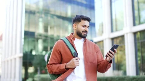 Smiling student with a backpack uses a mobile phone while walking in the campus  Stock Footage 315559311