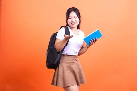 Smiling student with black backpack, white shirt and a blue book posing in .. Stock Photos