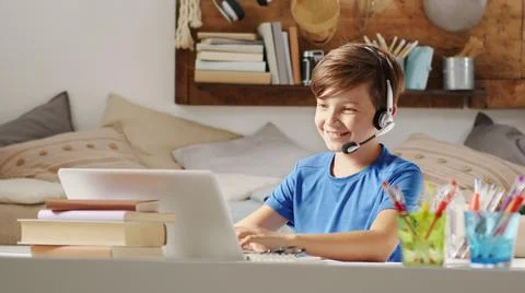 Smiling student boy studying on the computer at remote school on the web, con Stock Photos