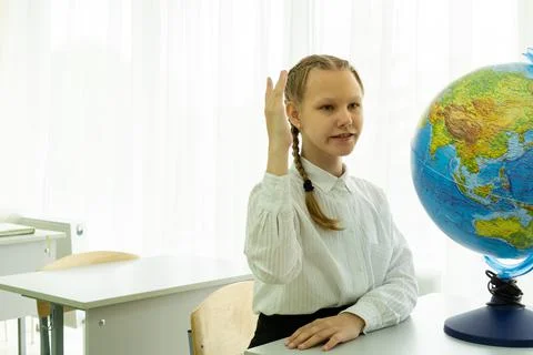 A smiling student giving an answer in class with her hand raised is sitting at a 写真素材