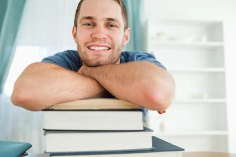 Smiling student leaning on a stack of books 写真素材