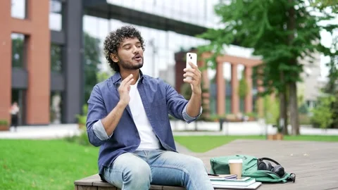 Smiling student talking on a video call using a mobile phone while sitting  Stock Footage 302472007