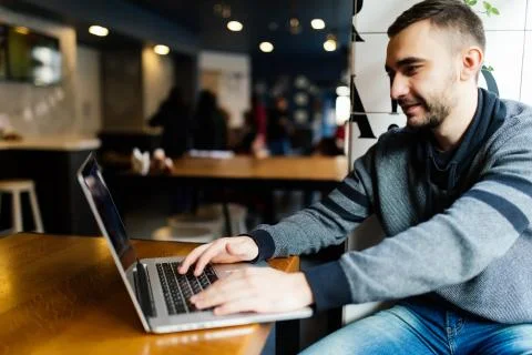 Smiling student using laptop in cafe at the university. Freelancer working wi Stock Photos