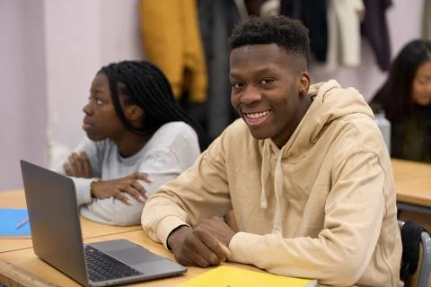 Smiling student using laptop in classroom with classmates attending lesson Stock Photos