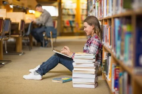 Smiling student using laptop on library floor 스톡 사진