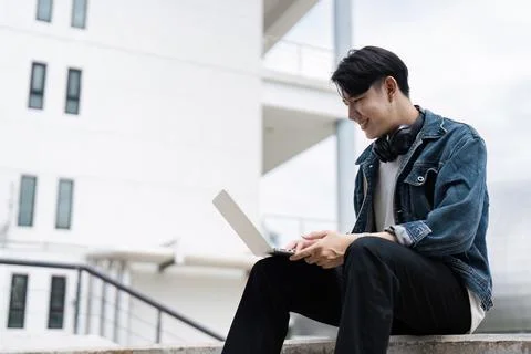Smiling Student Using Laptop Outdoors on Campus, Wearing Headphones and Casual Stock Photos