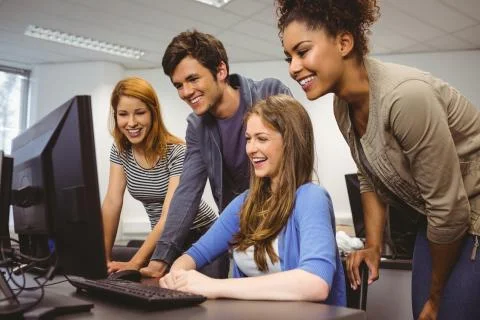 Smiling students sitting at desk using computer together Stock Photos