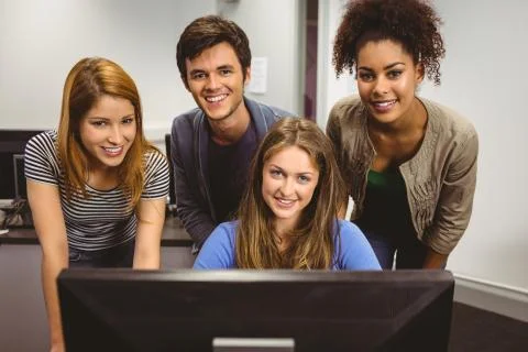 Smiling students using computer together looking at camera Stock Photos