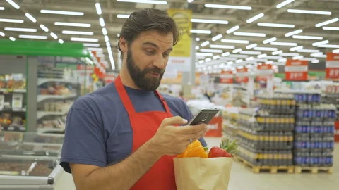 Smiling supermarket employee using mobile phone and holding shopping bag in Stock Footage 92546491