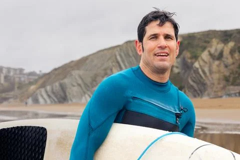 Smiling surfer by the sea with cliffs in background, copy space. Stock Photos