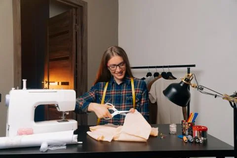 A smiling tailor look at the camera cut out a sketch of the garment. Seamstre Stock Photos