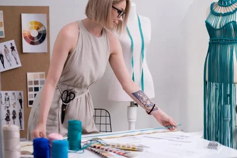 Smiling tailor measures green thread with tape on table in fashion studio woman Stock Photos