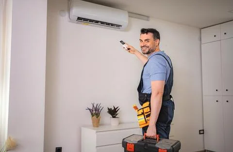 Smiling technician testing an air conditioner with a remote control Stock Photos