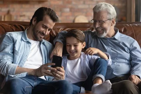 Smiling three generations of men use smartphone together Foto stock
