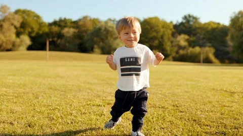 Smiling toddler takes first steps on a sunny meadow Stock Footage 310439013
