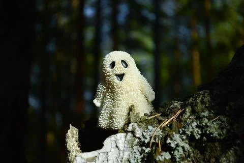 A smiling toy ghost stands on the bark of a tree in chiaroscuro Foto stock
