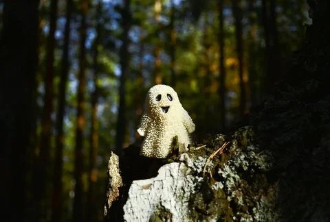 A smiling toy ghost stands on the bark of a tree in chiaroscuro Stock-Fotos