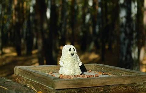 Smiling toy ghost stands sideways on a wooden plank in the autumn forest Stock Photos