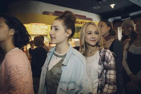 Smiling tween girls waiting in queue in movie theater lobby Stock Photos