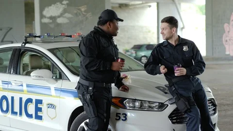 Smiling two policemen drinking coffee and eating donut with appetite talk near Stock Footage 112956386