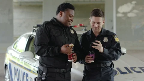 Smiling two policemen drinking coffee and eating donut use phone talk near Stock Footage 112957252