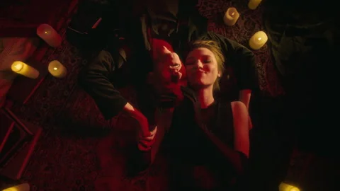 Smiling Vampire Lovers Lying on Patterned Rug Among Glow of Numerous Lit Candles Stock Footage 303983299