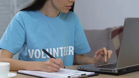 Smiling volunteer comparing data on laptop and in written list looking to camera Stock Footage 113672988