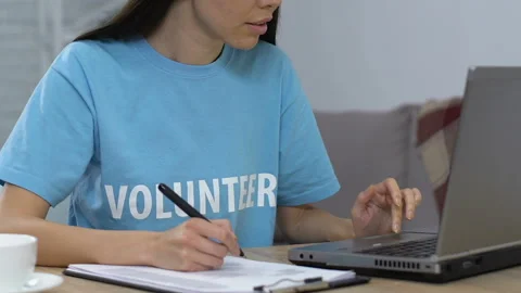 Smiling volunteer comparing data on laptop and in written list looking to camera Stock Footage 113680887