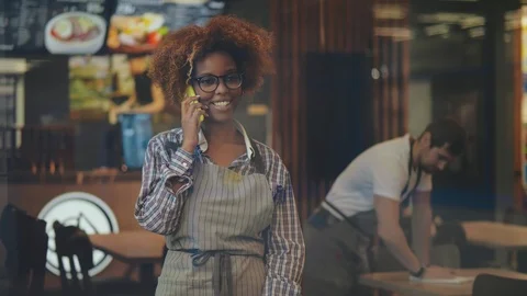 Smiling waitress looking away while talking on mobile phone in cafe Stock Footage 123438609