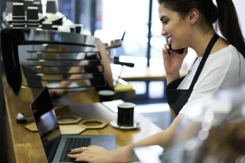 Smiling waitress talking on cellular with clients reserving table in coffee shop Stock Photos