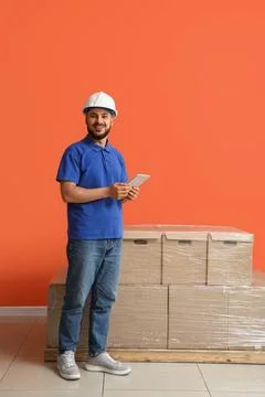 Smiling warehouse worker in hard hat holding digital tablet next to stacked c Stock Photos