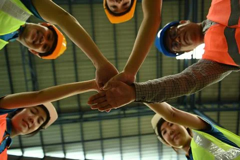 Smiling warehouse workers team stacking hands together bottom view. Unity Stockfoto's