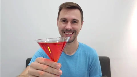 Smiling white man holding a red cocktail in a martini glass giving cheers Stock Footage 282610704