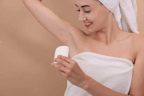 Smiling woman applying solid deodorant on beige background Stockfoto's