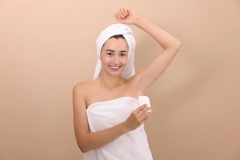 Smiling woman applying solid deodorant on beige background Stockfoto's
