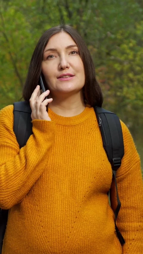 Smiling woman with backpack talking on the phone while walking through an Vidéo 342908360