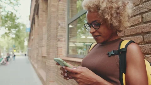 Smiling woman with backpack texting on mobile phone while standing outside Stock Footage 255505618