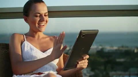Smiling woman chatting on tablet while relaxing on terrace HD Stock Footage 10888669