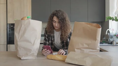 Smiling Woman Checking Receipt At Kitchen Table With Grocery Bags Stock Footage 311278343