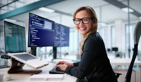 Smiling Woman Coder Managing Screens In Bright Office Setting. Photos