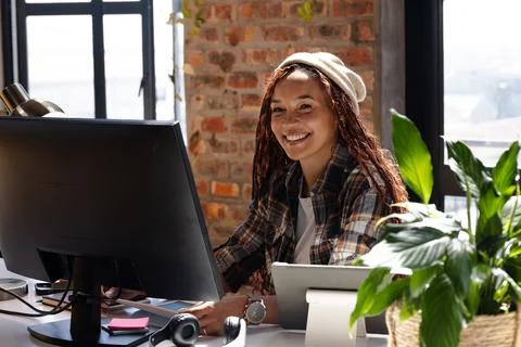 Smiling woman coding at desk with computer and plants in modern office Foto stock