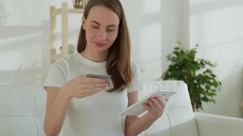 Smiling woman on the couch using a tablet and bank card makes online purchases 库存影片 150025820